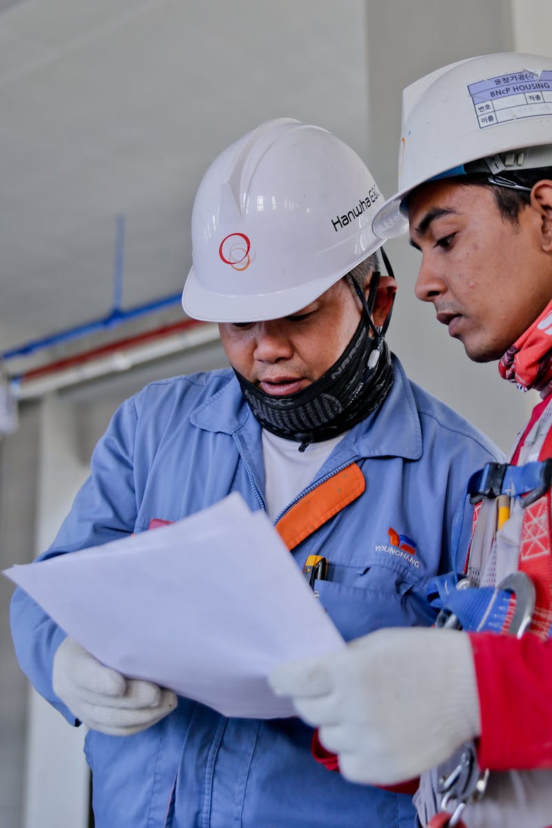 Two engineers in safety helmets reviewing construction plans at a worksite.